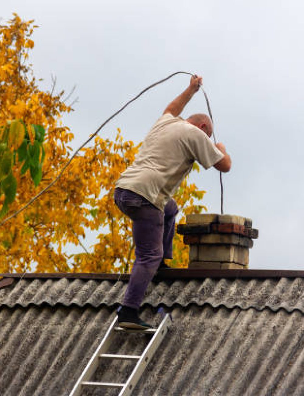 a male chimney sweep cleans the chimney from soot on the roof of a village house, preparation for the heating season