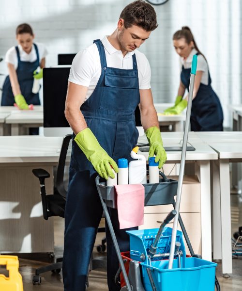 young-cleaner-standing-near-cart-with-cleaning-supplies.jpg